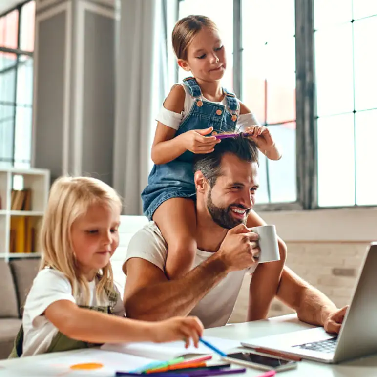 Father working on laptop at home with two young daughters, symbolizing family life and home buying in Tucson